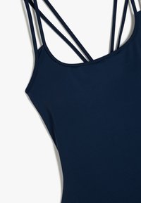 Granatowy top bez rękawów z podwójnymi cienkimi ramiączkami krzyżującymi się z tyłu, gładki materiał, zbliżenie na górną przednią część.