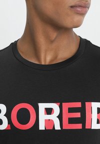 T-shirt in cotone nero con una stampa audace "BORED" rossa e bianca sul petto, collezione girocollo e maniche corte.