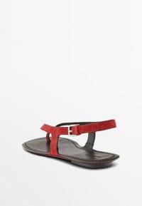 Rote Wildleder-Flatsandalen mit einem T-förmigen Design und einem silbernen Schnallen-Detail am Knöchelriemen. Schwarze Leder-Innensohle und minimalistisches Silhouette.