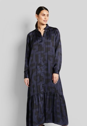 Langärmliges Kleid mit navyblauem Grund und einem geometrischen Muster in Hellblau. Aus glattem Stoff gefertigt, hat es einen gestuften Saum und einen Kragen-Ausschnitt.