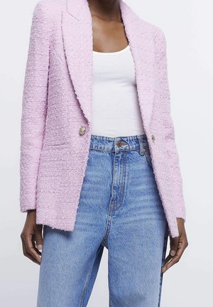 Femme portant un blazer texturé lavande sur un débardeur blanc et un jean taille haute bleu clair, debout devant un fond uni.