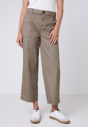 Pantaloni beige a gamba larga realizzati in tessuto leggero, con chiusura a bottoni, tasche laterali e orlo corto, abbinati a sneaker bianche.
