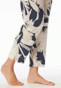 Leichte gemusterte Hose mit einem creme- und marineblauen Design, das einen geraden Schnitt und seitliche Schlitze am Saum zeigt. Barfuß-Modell sichtbar.