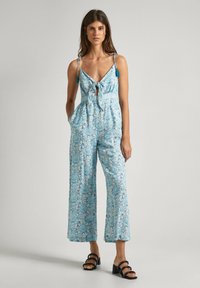 Blauwe gestipte jumpsuit met dunne schouderbanden, een strikdetail aan de voorkant, een wijde broekspijp en zakken. Kenmerkt zich door een gestructureerde stof en contrasterende kwastjes.
