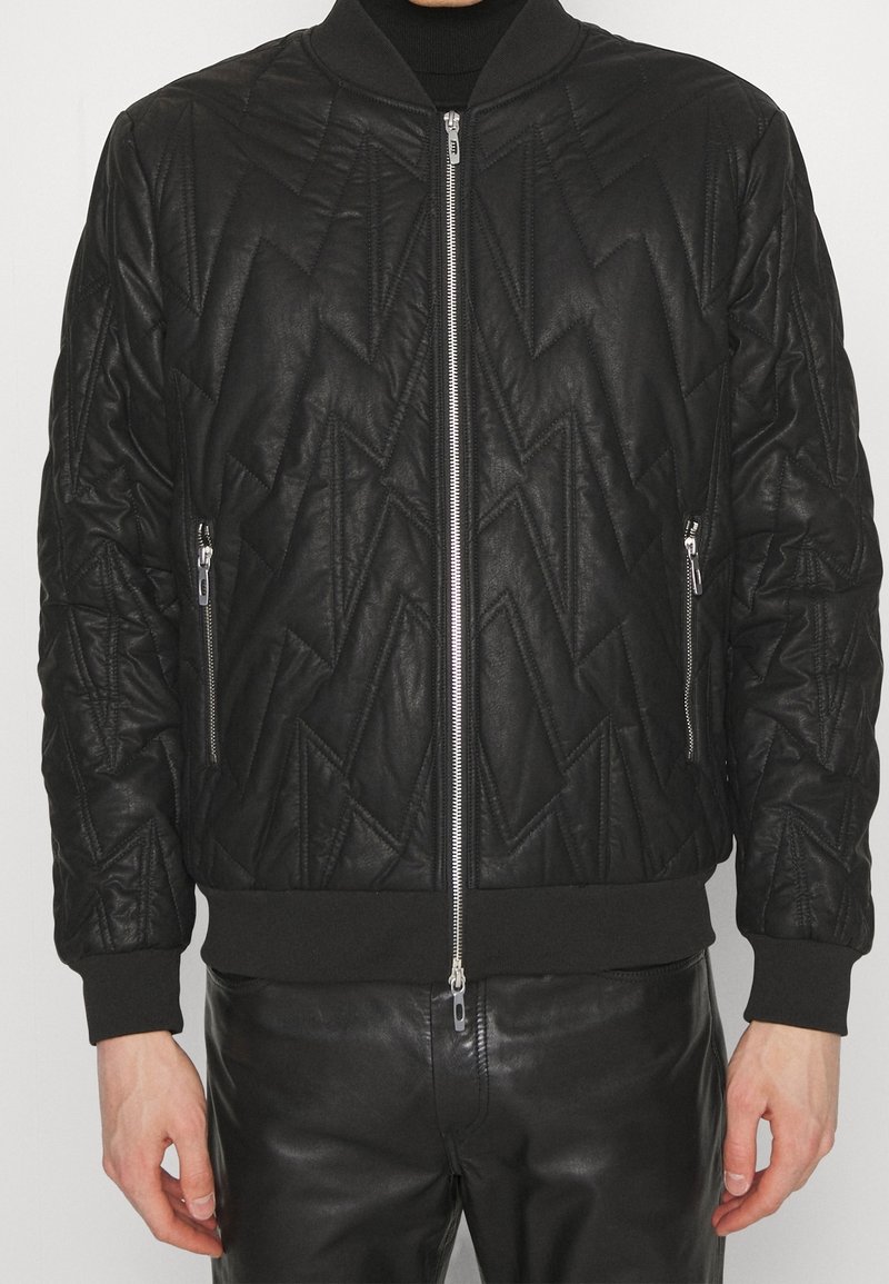 Veste bomber noire avec un motif en zigzag matelassé, fermeture éclair à l'avant, poches latérales et poignets côtelés. Fabriquée en tissu texturé avec une finition lisse.