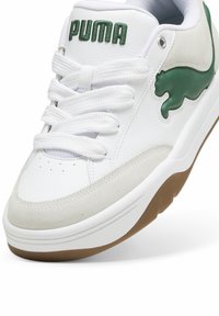 Białe skórzane sneakersy z zielonymi akcentami, z szarym zamszowym panelem bocznym i teksturowaną gumową podeszwą. Branding widoczny na języku.