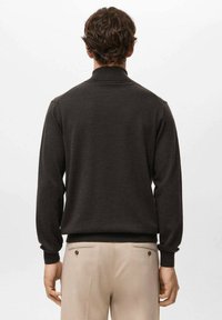 Ciemnobrązowy dzianinowy sweter z wysokim kołnierzem, długimi rękawami i ściągaczami, zestawiony z jasnobeżowymi spodniami z tylnymi kieszeniami.