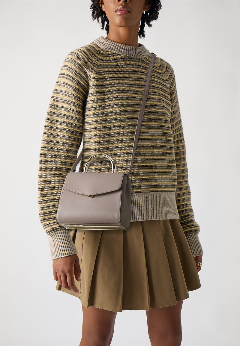 Grå læder håndtaske med en guld-tone håndtag, med en frontklap lukning, parret med en stribet sweater og en plisseret beige nederdel.
