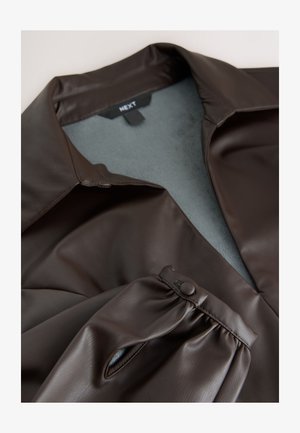 Brun skinnimitation skjorta med krage och knappad manschett. Insidan är mjukt grått tyg, med en len yta och strukturerad design.
