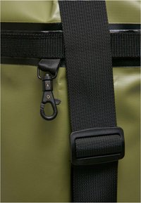 Grønn vanntett bag med svart stropp, solid spenne og detalj med metalldel, laget av glatt teksturert materiale og forsterkede sømmer.
