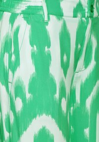 Grön och vit mönstrad tyg med en vågformad design, slät textur och en skräddarsydd passform med sidofickor.