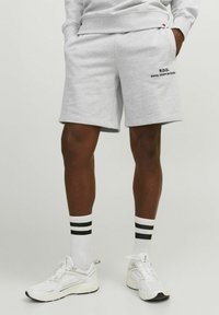Gray sweatshirt shorts in a soft fabric with side pockets. Features a black printed logo. Paired with white sneakers and striped socks.