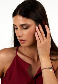 Bracciale in tonalità argento e oro con una fascia testurizzata, caratterizzato da charm. Il modello ha lunghi capelli scuri e indossa un top senza maniche color bordeaux.
