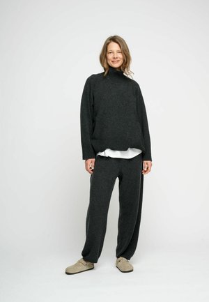 Dark gray knitted sweater with a high collar, paired with matching loose-fitting gray trousers and beige slip-on shoes. Smooth texture.