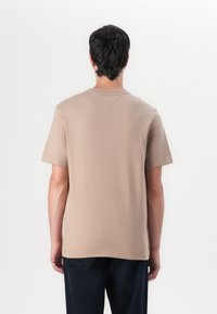 T-shirt marron clair à manches courtes en coton doux. Présente un col rond et une coupe droite avec un minimum de détails au dos.
