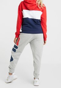 Röd, vit och marinblå färgblockerad hoodie med framficka, i kombination med ljusgråa sweatpants med abstrakta blå och röda mönster.