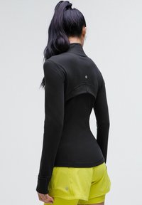 Haut de sport noir à manches longues avec un col haut, design ajusté et découpe au dos, associé à un short jaune vif.
