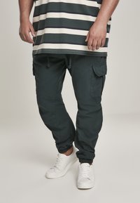Donkergroene cargobroek met zijzakken en elastische boorden, gecombineerd met witte sneakers. De top heeft horizontale strepen in marineblauw en roomkleur.