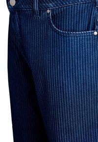 Tumedat sinised teksapüksid, millel on peen vertikaalne triipude muster, viie-tasku disain ja metallnupud vööl.