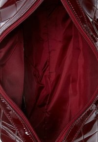 Intérieur brillant de sac à main bourgogne avec une texture lisse, doté d'une fermeture à glissière et d'une doublure en tissu uni dans une teinte assortie.