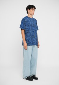 Zils leoparda raksts, īsām piedurknēm, krekls ar brīvu piegriezumu, apvienots ar gaiši ziliem platām kājām biksēm un melniem apaviem. Gluda auduma tekstūra.