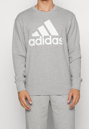 Mand iført grå Adidas sweatshirt og matchende sweatpants, forfra, med Adidas logo centreret på brystet.