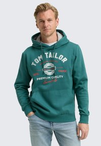 Sudadera con capucha color verde azulado con bolsillo delantero, que presenta texto en blanco y rojo. Tejido suave con un ajuste casual, capucha con capas y puños de canalé.