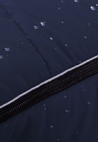 Marineblauwe geborduurde stof met waterdruppels, voorzien van een zwarte rits en grijze bies langs de rand, met een gladde textuur en glans.