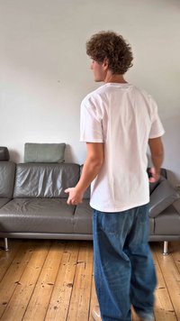 Γκρι δερμάτινος καναπές με ομαλή υφή, μεταλλικά πόδια και διακοσμητικό μαξιλάρι με σχέδιο. Τα πατώματα είναι από ανοιχτό ξύλο με εμφανή νερά. Φοριέται καθημερινή ενδυμασία.