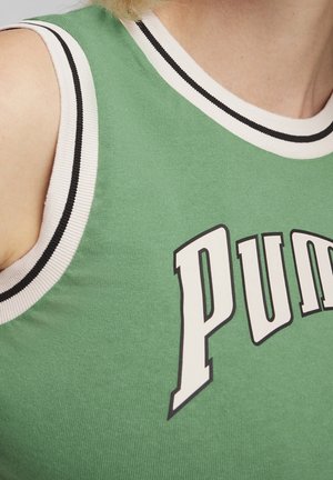 Chemise verte sans manches avec bordure blanche et noire portée par une personne, arborant de grandes lettres blanches "PUM" à l'avant.