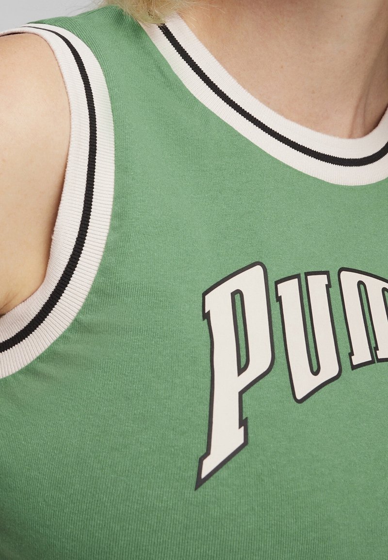 Chemise verte sans manches avec bordure blanche et noire portée par une personne, arborant de grandes lettres blanches "PUM" à l'avant.