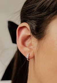 Orecchini d'argento con design a forma di stella, caratterizzati da piccoli zirconi trasparenti, attaccati a un cerchio circolare. Indossati sull'orecchio di una persona.