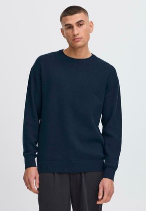 Pull en maille bleu marine avec un col rond, des épaules tombantes et des bords-côtes aux poignets et à l'ourlet ; texture lisse et coupe décontractée.
