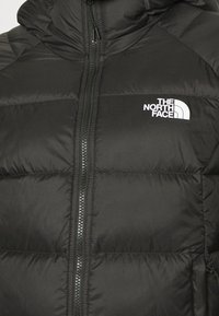 Veste matelassée noire avec fermeture éclair avant et logo blanc "The North Face" sur la poitrine gauche en haut.