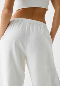 Vita linnbyxor med elastisk midja och sidofickor; lättviktsmaterial med en mjuk textur, utformade för komfort och enkelhet.