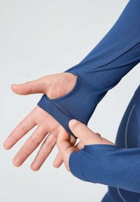 Top de tejido azul de mangas largas con orificios para los pulgares en los puños, material texturizado y detalle de costura en contraste a lo largo de las costuras.