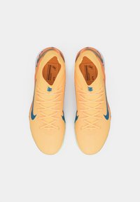 Pár žluto-oranžových tenisek Nike s modrými logy swoosh, šňůrky uvázané, a vzorované podrážky, pohled shora na bílém pozadí.