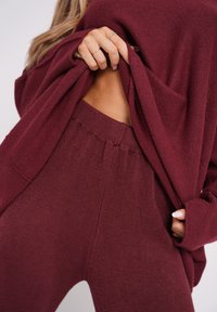 Bordowy sweter o luźnym kroju i okrągłym dekolcie, nałożony na dopasowane spodnie w tym samym kolorze z elastycznym paskiem i miękką teksturą.