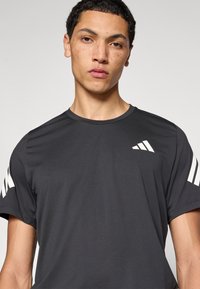 Must athletiline T-särk lühikeste varrukatega. Õlgadel valged diagonaaltriibud ja rinnal väike valge logo. Sile tekstuur.