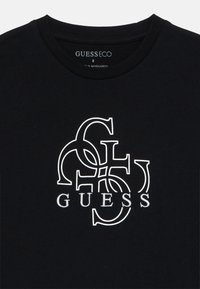 Black t-shirt with white interlocking GS logo above the word "GUESS" in capital letters centered on the chest.