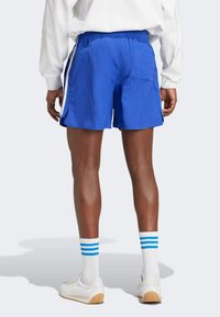 Modré sportovní kraťasy vyrobené z lehkého materiálu s elastickým pasem, mají boční kapsy a kontrastní bílé lemování po stranách.