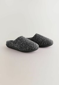 Grå strikkede hjemmesko med en tekstureret overdel og en sort gummisål, med åben bag og rund tådesign.