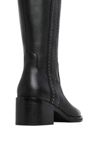 Bota negra de cuero hasta la rodilla con tacón apilado, que presenta filas verticales de studs decorativos a lo largo del costado. Textura suave y diseño ajustado.