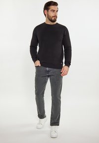Fekete kötött pulóver kerek nyakkal, szürke farmernadrággal párosítva. A modellen fehér sportcipők vannak, ami egy laza öltözetet mutat.