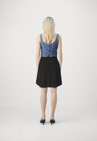 Farmer cropped top, állítható hátrésszel és fekete pliszírozott szoknyával. A modellen fekete magassarkú mules cipők vannak. Egyszerű dizájn, könnyű textúra és kontrasztos színek.