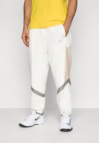 Λευκό αθλητικό παντελόνι με γκρι λεπτομέρειες και πλαινά από δίχτυ, διαθέτει ελαστική μέση και τελειώματα στα μπατζάκια, σε συνδυασμό με λευκά παπούτσια Nike.