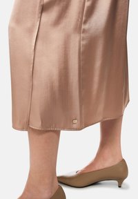 Satin midi skirt in soft pink with a smooth texture, featuring a gold accent button at hem. Paired with beige pointy-toed heels.