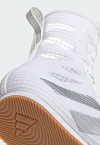Detailný záber bielej športovej obuvi s priesvitným textúrovaným zvrškom, striebornými akcentmi, pútkom a svetlohnedou gumovou podrážkou s dezénom.