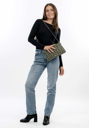 Top nero a maniche lunghe, jeans blu a vita alta e stivali neri con tacco alla caviglia. Tiene una borsa a tracolla verde e nera con motivo testurizzato.