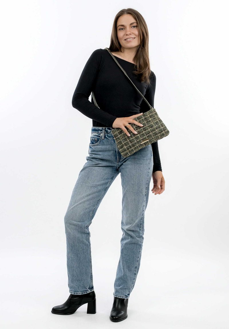 Top nero a maniche lunghe, jeans blu a vita alta e stivali neri con tacco alla caviglia. Tiene una borsa a tracolla verde e nera con motivo testurizzato.